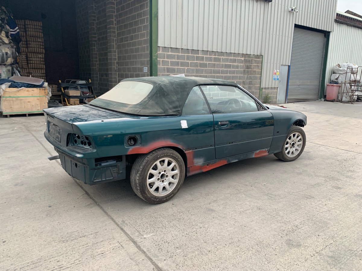 Green BMW 318i Convertible mid-restoration with primer patches, parked outside a workshop